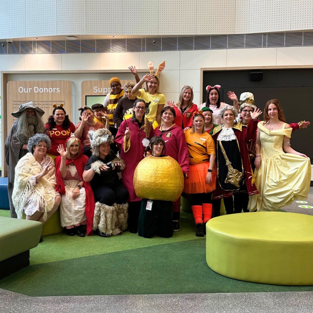 A large group of teachers wearing an array of colourful book themed costumes pose for a group photograph.