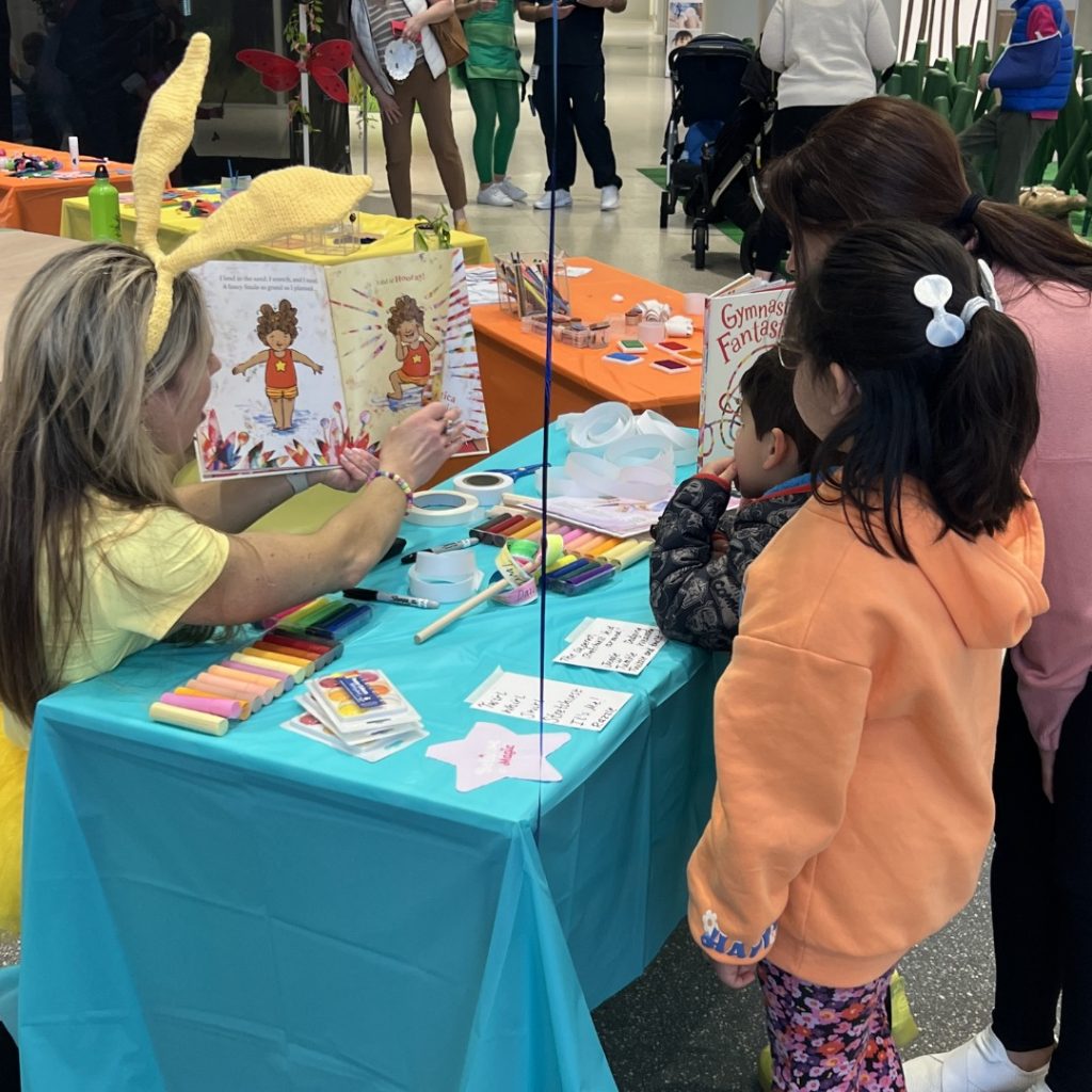 A teacher in a yellow bunny costume reads a book to a young family.