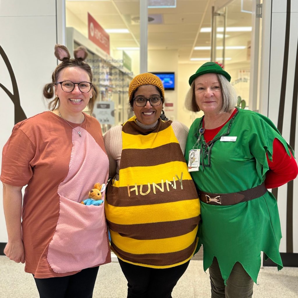 A woman in a green Peter Pan costume poses for a photo with two women dressed as Kanga and a pot of honey.